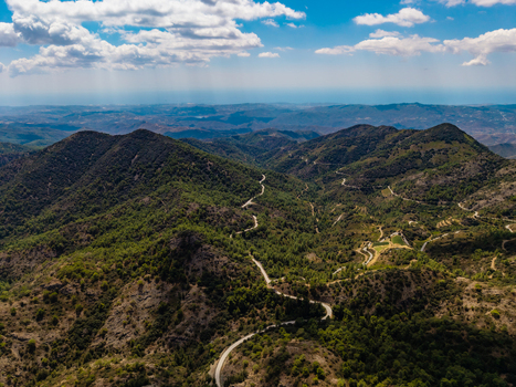 Aerial view of Kionia mountain range featuring a winding road through lush green hills and rugged terrain under a blue sky in Lazanias Lefkosia Cyprus. Aerial view of Kionia mountain range featuring a winding road through lush green hills and rugged terrain under a blue sky in Lazanias Lefkosia Cyprus.