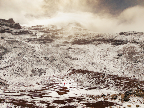 Aerial view of the snow covered slopes of Volcano Chimborazo with two small figures standing in the vast rocky landscape in Guano Chimborazo Ecuador. Aerial view of the snow covered slopes of Volcano Chimborazo with two small figures standing in the vast rocky landscape in Guano Chimborazo Ecuador.