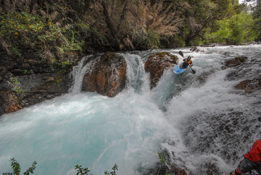 View of a kayaker navigating the turquoise rapids of the Rio Manso waterfall surrounded by lush forest in San Carlos de Bariloche Rio Negro Argentina. View of a kayaker navigating the turquoise rapids of the Rio Manso waterfall surrounded by lush forest in San Carlos de Bariloche Rio Negro Argentina.