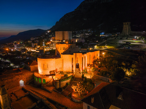 Aerial view of the illuminated Kruje Castle and Skanderbeg Museum at night with the city lights and mountain in the background in Kruje Durres County Albania.