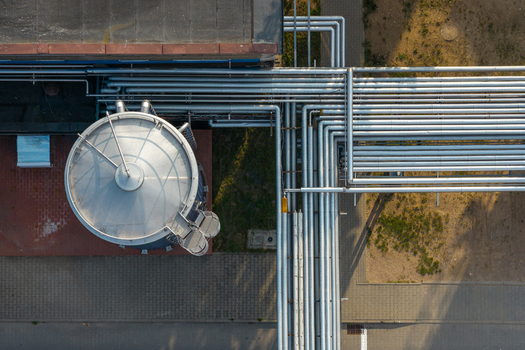 Aerial view of raw milk storage tanks connected to a complex network of stainless steel industrial pipes at a processing facility in Poland.