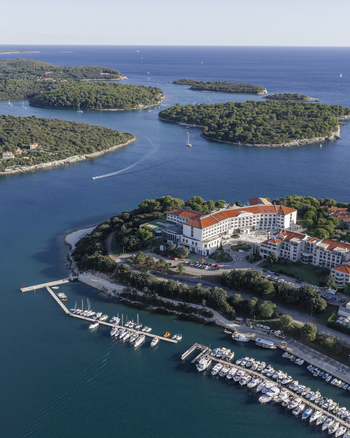 Aerial view of a coastal resort with a marina filled with boats surrounded by lush green islands and the blue Adriatic Sea in Pula Istarska zupanija Croatia.