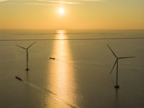 Aerial view of offshore wind turbines and cargo ships on the calm sea during a golden sunset in Netherlands. Aerial view of offshore wind turbines and cargo ships on the calm sea during a golden sunset in Netherlands.