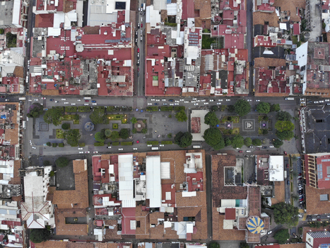 Aerial view of the historic Centro plaza featuring lush green trees paved walkways and surrounding colonial style buildings with red tiled roofs in Uruapan Michoacan Mexico.