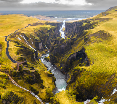 Aerial view of a river snaking through a deep canyon with mossy green slopes under a dramatic sky Fjaðrárgljúfur Skaftárhreppur Iceland. Aerial view of a river snaking through a deep canyon with mossy green slopes under a dramatic sky Fjaðrárgljúfur Skaftárhreppur Iceland.