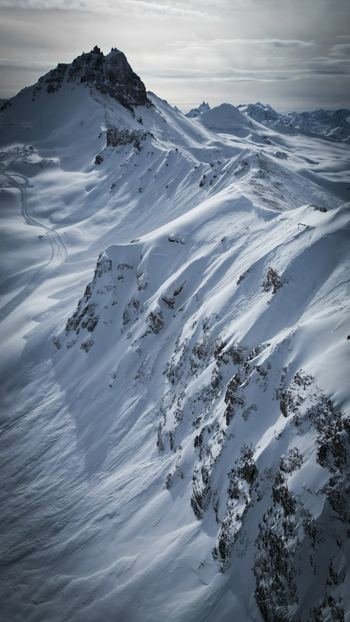 Aerial view of snow laden peaks casting long shadows with the stark contrast between the sunlit ridges and the deep blue hollows creating a dramatic winter landscape Anniviers Switzerland.