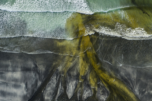 Aerial view of Talisker Bay Beach featuring dark volcanic sand and yellow river water mixing with crashing ocean waves Isle of Skye Scotland United Kingdom. Aerial view of Talisker Bay Beach featuring dark volcanic sand and yellow river water mixing with crashing ocean waves Isle of Skye Scotland United Kingdom.