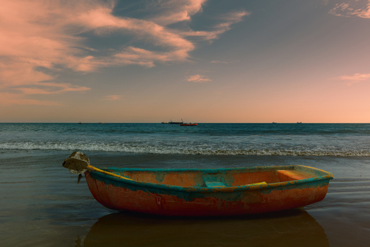 View of a weathered colorful wooden boat resting on the wet sand of Kund Malir Beach at sunset with gentle waves in the background in Kund Malir Balochistan Pakistan.
