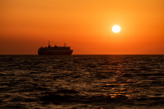 View of a ferry sailing on the sea during a vibrant golden sunset in Greece. View of a ferry sailing on the sea during a vibrant golden sunset in Greece.