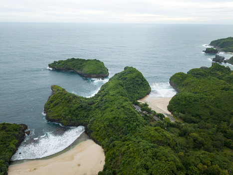 Aerial view of lush green headlands meeting the turquoise sea waves crashing on the sandy beach Sedahan Beach Gunungkidul Regency Special Region of Yogyakarta Indonesia. Aerial view of lush green headlands meeting the turquoise sea waves crashing on the sandy beach Sedahan Beach Gunungkidul Regency Special Region of Yogyakarta Indonesia.