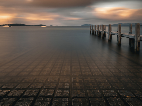 View of the wooden jetty extending into the calm waters of the bay at sunset with a paved foreground in Little Grove Western Australia Australia. View of the wooden jetty extending into the calm waters of the bay at sunset with a paved foreground in Little Grove Western Australia Australia.