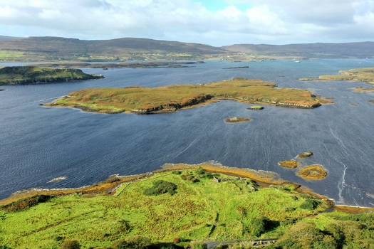 Aerial view of the coastal landscape near Dunvegan Castle and Gardens with green islands rocky shorelines and deep blue waters in Isle of Skye Scotland United Kingdom. Aerial view of the coastal landscape near Dunvegan Castle and Gardens with green islands rocky shorelines and deep blue waters in Isle of Skye Scotland United Kingdom.
