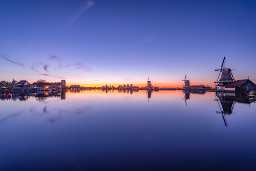 View of traditional Dutch windmills reflected in the calm water of a canal during a vibrant sunset in Nederland.