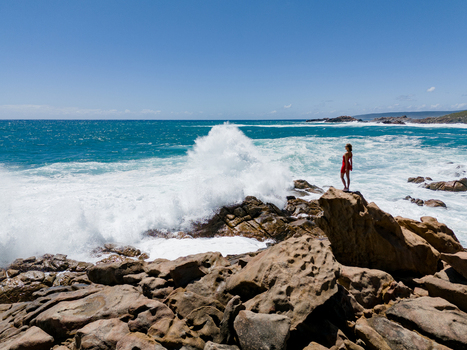 Aerial view of a woman in a red dress standing on the rocky coastline at Injidup Natural Spa with turquoise waves crashing against the shore Yallingup Western Australia Australia. Aerial view of a woman in a red dress standing on the rocky coastline at Injidup Natural Spa with turquoise waves crashing against the shore Yallingup Western Australia Australia.
