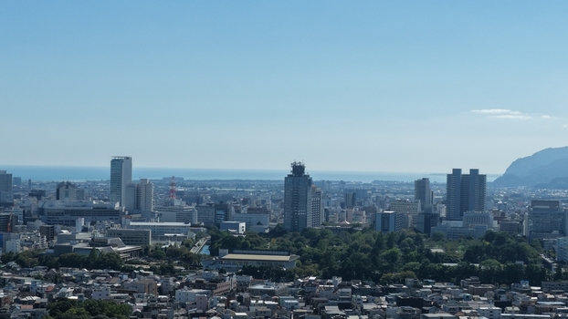 Aerial view of the cityscape of Shizuoka featuring high rise buildings lush green parks and the distant coastline of Suruga Bay under a clear blue sky Shizuoka Shizuoka Japan.