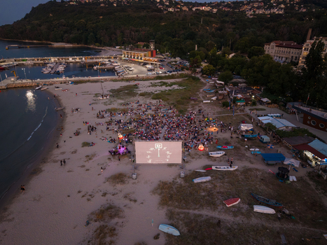 Aerial view of The Quarantine Film Festival with a large screen and audience gathered on the beach at dusk near the harbor in Asparuchovo Varna Bulgaria.