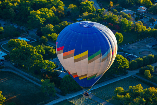 Albuquerque United States 11 October 2017 View of a vibrant hot air balloon drifts serenely above a patchwork of green trees and buildings contrasting against the blue sky. Albuquerque United States 11 October 2017 View of a vibrant hot air balloon drifts serenely above a patchwork of green trees and buildings contrasting against the blue sky.