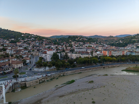 Aerial view of the historic town of Berat with its traditional stone houses the Osum River and surrounding hills under a soft sunset sky in Berat Berat County Albania.