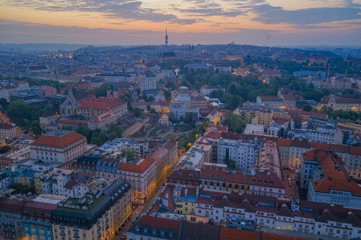 Aerial view of the historic city of Prague at sunset featuring the Zizkov Television Tower rising above the dense urban rooftops and glowing street lights in Prague Prague Czechia.