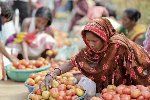Odisha India 26 March 2026 View of a woman in a floral hijab selecting vibrant tomatoes at a bustling market with blurred figures adding to the vibrant atmosphere. Odisha India 26 March 2026 View of a woman in a floral hijab selecting vibrant tomatoes at a bustling market with blurred figures adding to the vibrant atmosphere.