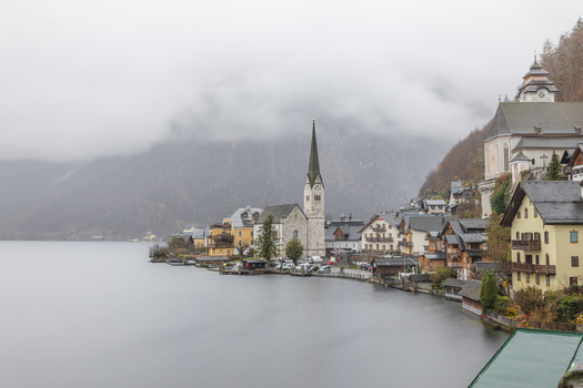 View of the iconic Lutheran Church and traditional alpine houses along the misty shores of Lake Hallstatt under a foggy mountain backdrop in Hallstatt Upper Austria Austria. View of the iconic Lutheran Church and traditional alpine houses along the misty shores of Lake Hallstatt under a foggy mountain backdrop in Hallstatt Upper Austria Austria.