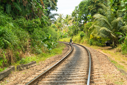 View of a curved railway track surrounded by lush tropical vegetation and palm trees with people walking in the distance Mirissa Southern Province Sri Lanka. View of a curved railway track surrounded by lush tropical vegetation and palm trees with people walking in the distance Mirissa Southern Province Sri Lanka.