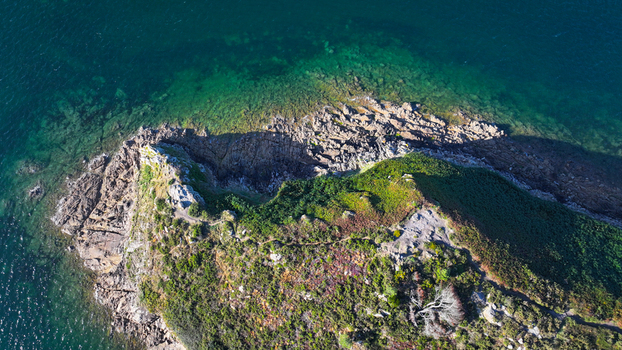 Aerial view of a rugged verdant headland reaching into the shimmering emerald and sapphire waters Carantec Bretagne France.