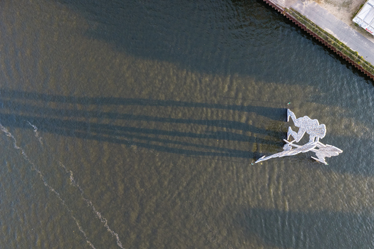 Aerial view of the Molecule Men sculpture standing in the Spree river casting long shadows on the water in Berlin Berlin Germany. Aerial view of the Molecule Men sculpture standing in the Spree river casting long shadows on the water in Berlin Berlin Germany.
