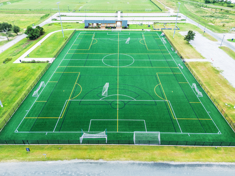 Aerial view of nCino Sports Park featuring a green synthetic soccer field with white and yellow markings surrounded by grass fields in Wilmington North Carolina United States. Aerial view of nCino Sports Park featuring a green synthetic soccer field with white and yellow markings surrounded by grass fields in Wilmington North Carolina United States.