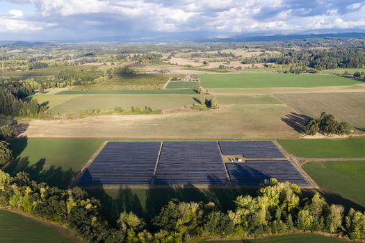 Aerial view of a solar farm with rows of photovoltaic panels situated in a rural landscape surrounded by green fields and trees in Woodburn Oregon United States. Aerial view of a solar farm with rows of photovoltaic panels situated in a rural landscape surrounded by green fields and trees in Woodburn Oregon United States.