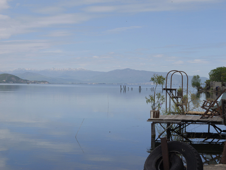 View of a wooden pier with a metal structure extending into the calm waters of Lake Ohrid with distant mountains under a clear sky in Lin Korce County Albania.