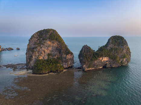 Aerial view of towering limestone cliffs rise majestically from the turquoise waters their rugged surfaces softened by patches of verdant vegetation Krabi Thailand.