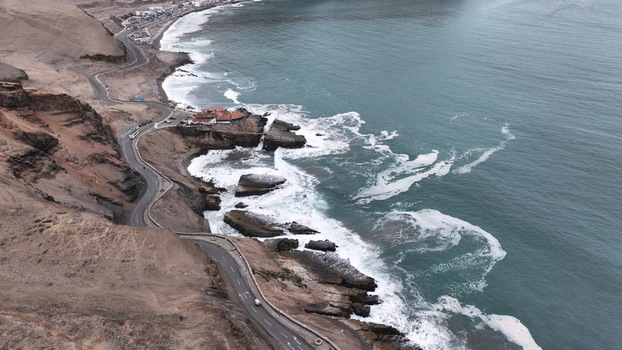Aerial view of the coastal cliffs and winding road in Barranco featuring crashing waves against the rocky shoreline and the Pacific Ocean in Barranco Lima Province Peru.
