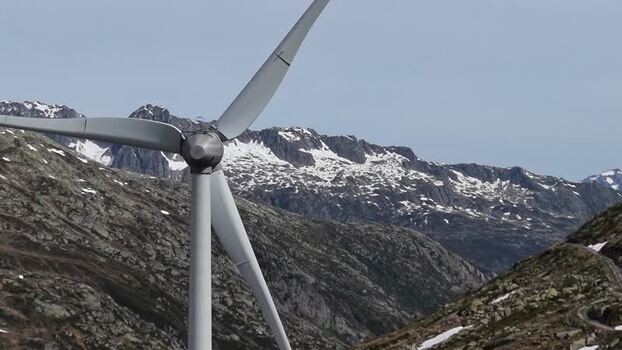 Aerial view of a large wind turbine at San Gottardo Wind Farm with snow capped mountains and rocky slopes in the background in Airolo Ticino Switzerland.