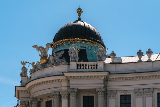 View of the ornate dome of the Hofburg Palace featuring intricate sculptures and gold detailing against a clear blue sky in Vienna Vienna Austria. View of the ornate dome of the Hofburg Palace featuring intricate sculptures and gold detailing against a clear blue sky in Vienna Vienna Austria.