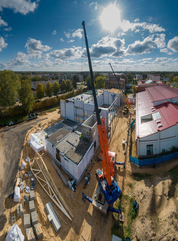 Aerial view of a construction site with a large orange mobile crane lifting concrete panels building materials and a nearby structure with a red roof under a sunny sky in Latvia. Aerial view of a construction site with a large orange mobile crane lifting concrete panels building materials and a nearby structure with a red roof under a sunny sky in Latvia.