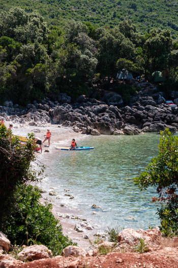 Jala Albania 12 June 2026 View of Aquarium Beach with people on paddleboards and tents nestled in the lush green trees along the rocky coastline.