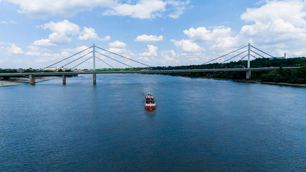 Aerial view of the Liberty Bridge spanning the Danube River with a boat cruising on the water under a cloudy sky in Novi Sad Vojvodina Serbia. Aerial view of the Liberty Bridge spanning the Danube River with a boat cruising on the water under a cloudy sky in Novi Sad Vojvodina Serbia.