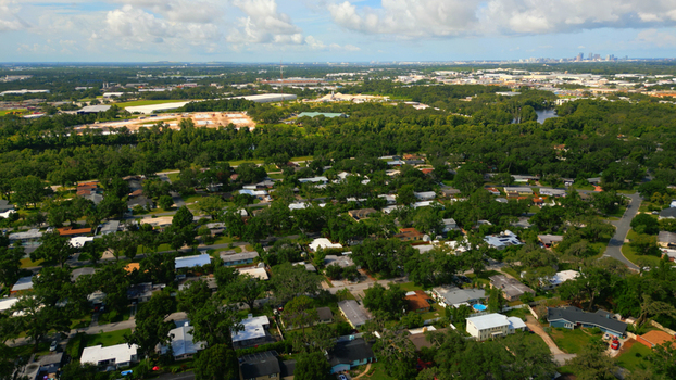 Aerial view of a suburban neighborhood with lush green trees residential houses and a distant city skyline under a blue sky in Tampa Florida United States. Aerial view of a suburban neighborhood with lush green trees residential houses and a distant city skyline under a blue sky in Tampa Florida United States.