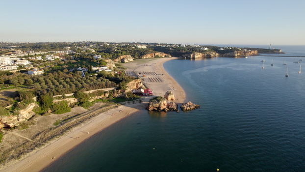 Aerial view of the sandy beach and rocky cliffs along the coastline of Ferragudo with calm sea and coastal buildings in Ferragudo Faro District Portugal.
