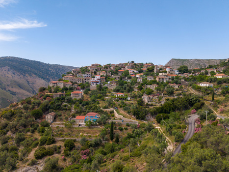 Aerial view of the historic stone houses and red tiled roofs of a hillside village nestled among lush green vegetation and winding roads in Qeparo Fshat Vlore County Albania. Aerial view of the historic stone houses and red tiled roofs of a hillside village nestled among lush green vegetation and winding roads in Qeparo Fshat Vlore County Albania.