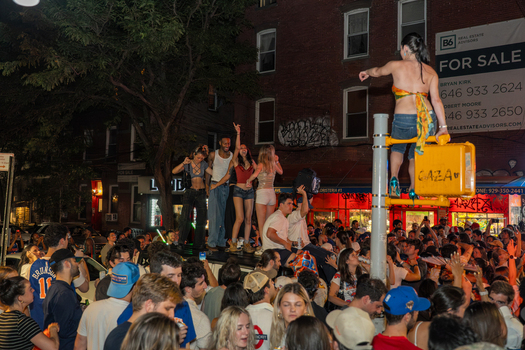 Williamsburg Brooklyn New York USA 14 June 2026 View of a large crowd celebrating in the street at night with people standing on a vehicle and a woman perched on a traffic light. Williamsburg Brooklyn New York USA 14 June 2026 View of a large crowd celebrating in the street at night with people standing on a vehicle and a woman perched on a traffic light.