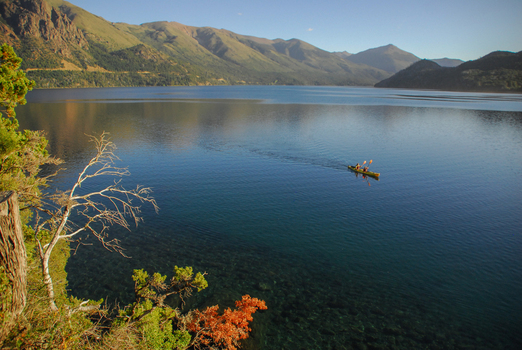 View of Nahuel Huapi Lake with two people in a yellow kayak on the calm blue water surrounded by high mountains in San Carlos de Bariloche Rio Negro Argentina. View of Nahuel Huapi Lake with two people in a yellow kayak on the calm blue water surrounded by high mountains in San Carlos de Bariloche Rio Negro Argentina.