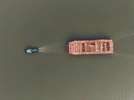 Aerial view of a tugboat pulling a large barge loaded with logs along the Mahakam River in Samarinda East Kalimantan Indonesia. Aerial view of a tugboat pulling a large barge loaded with logs along the Mahakam River in Samarinda East Kalimantan Indonesia.