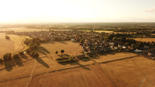 Aerial view of a residential town surrounded by golden agricultural fields and trees during the warm light of sunset in Windsor England United Kingdom. Aerial view of a residential town surrounded by golden agricultural fields and trees during the warm light of sunset in Windsor England United Kingdom.