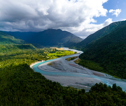 Aerial view of the Hokitika River carves through a landscape of dense emerald forests meeting rugged mountains under a dynamic sky Hokitika Gorge West Coast Region New Zealand. Aerial view of the Hokitika River carves through a landscape of dense emerald forests meeting rugged mountains under a dynamic sky Hokitika Gorge West Coast Region New Zealand.