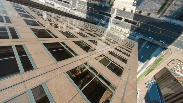 Aerial view of the glass and stone facade of a skyscraper in Downtown Los Angeles looking down at the busy city streets below in Los Angeles California United States.