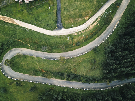 Aerial view of a serpentine asphalt ribbon carving through an emerald landscape bordered by crisp white barriers and contrasting dark green foliage Obudu Cross River Nigeria.