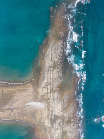 Aerial view of a rocky coastline with turquoise water and waves crashing against the shore in Costa Rica.