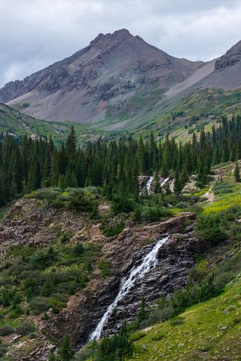 Aerial view of Mount Sneffels and the cascading waterfall in Yankee Boy Basin surrounded by evergreen forests and alpine meadows in the San Juan Mountains Ouray Colorado United States. Aerial view of Mount Sneffels and the cascading waterfall in Yankee Boy Basin surrounded by evergreen forests and alpine meadows in the San Juan Mountains Ouray Colorado United States.